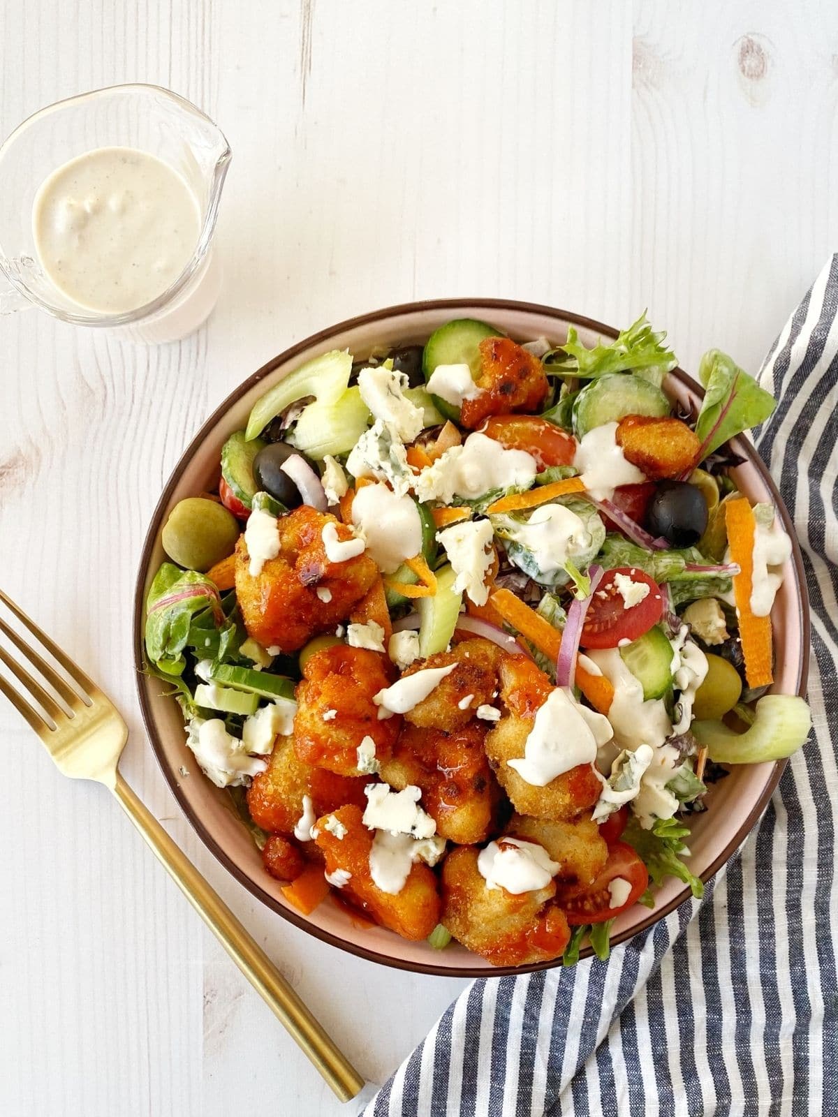 bowl of salad with pitcher of dressing and a fork