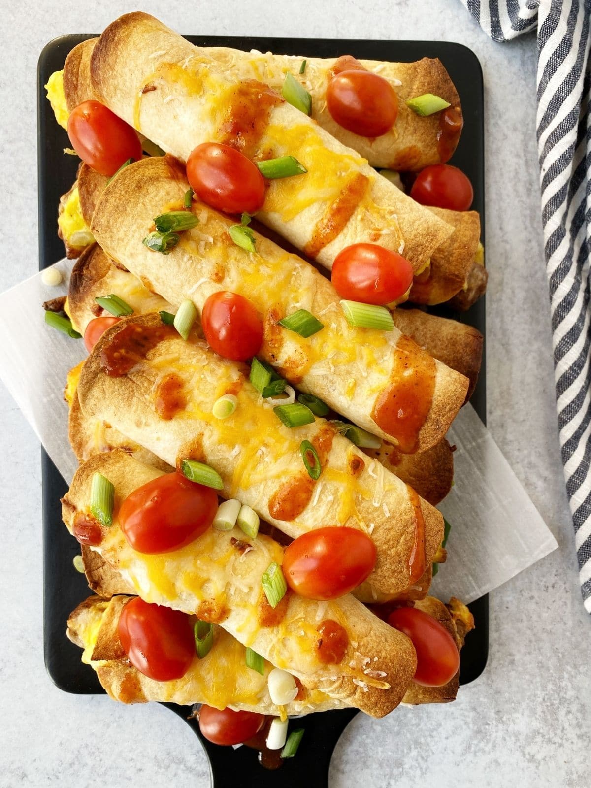 baked flautas garnished with cheese, sauce, and scallions on a board