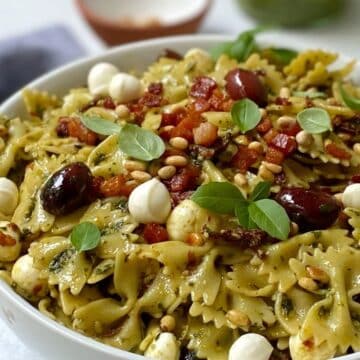 close up of white serving bowl with pancetta and pesto pasta.