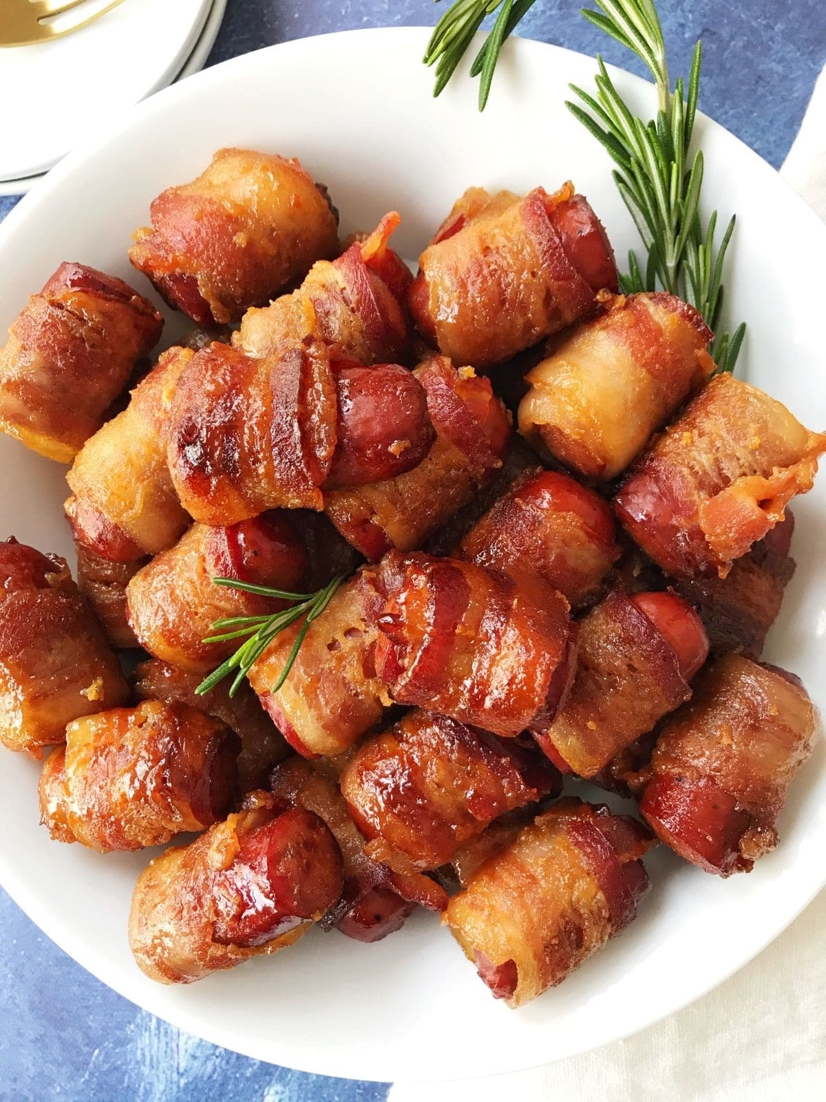 plate of bacon-wrapped sausages garnished with rosemary sprigs