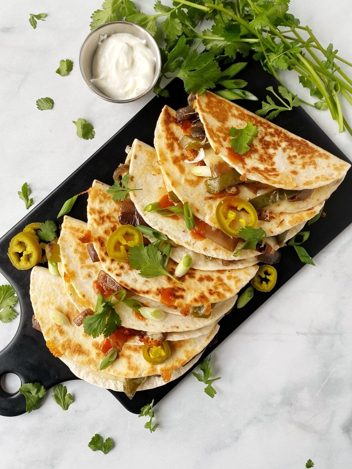 stack of quesadillas on a serving board with cilantro and sour cream