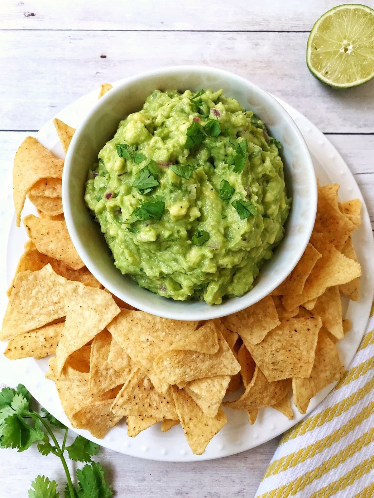 overhead of bowl of guacamole surrounded by chips, lime and cilantro