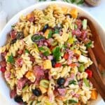 A bowl of pasta salad with serving utensils.