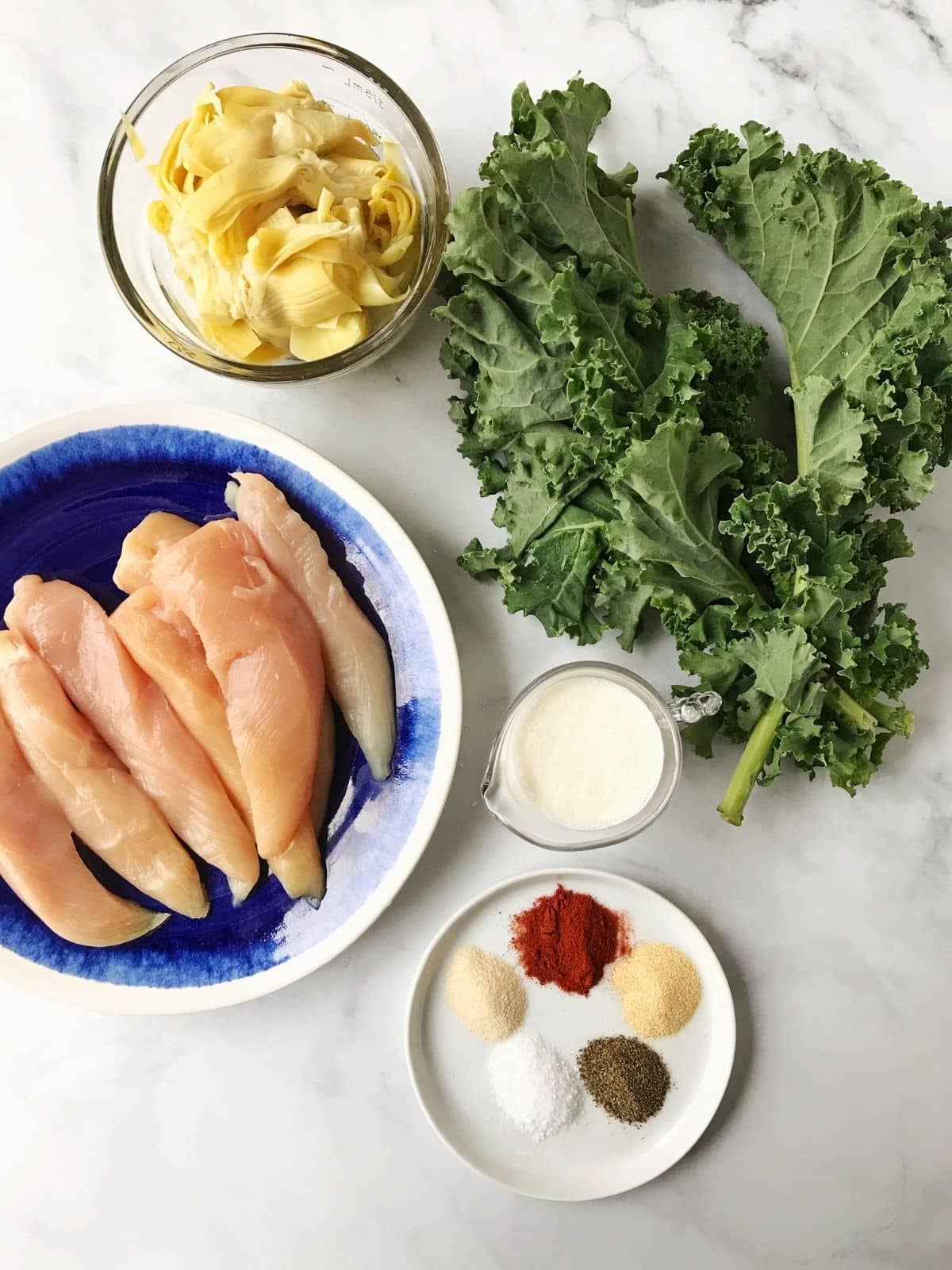 array of ingredients - chicken, kale, artichokes, seasonings, and cream