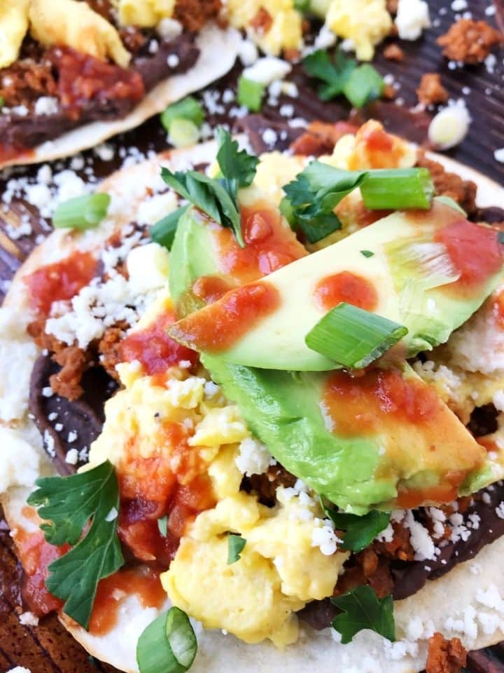 close up of tortilla topped with refried beans, eggs, avocado, and garnishes