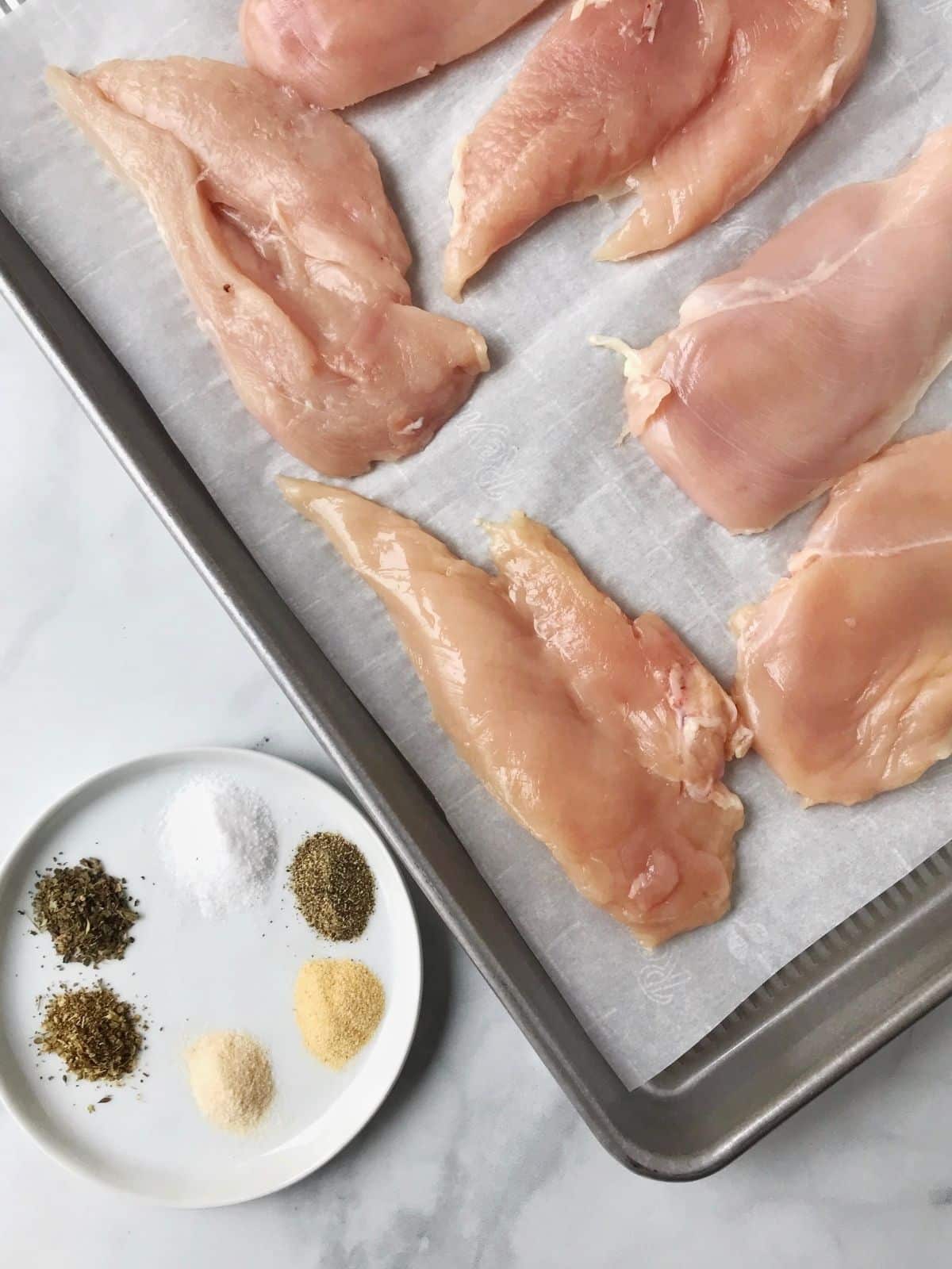 uncooked chicken on a sheet pan with spices for seasoning