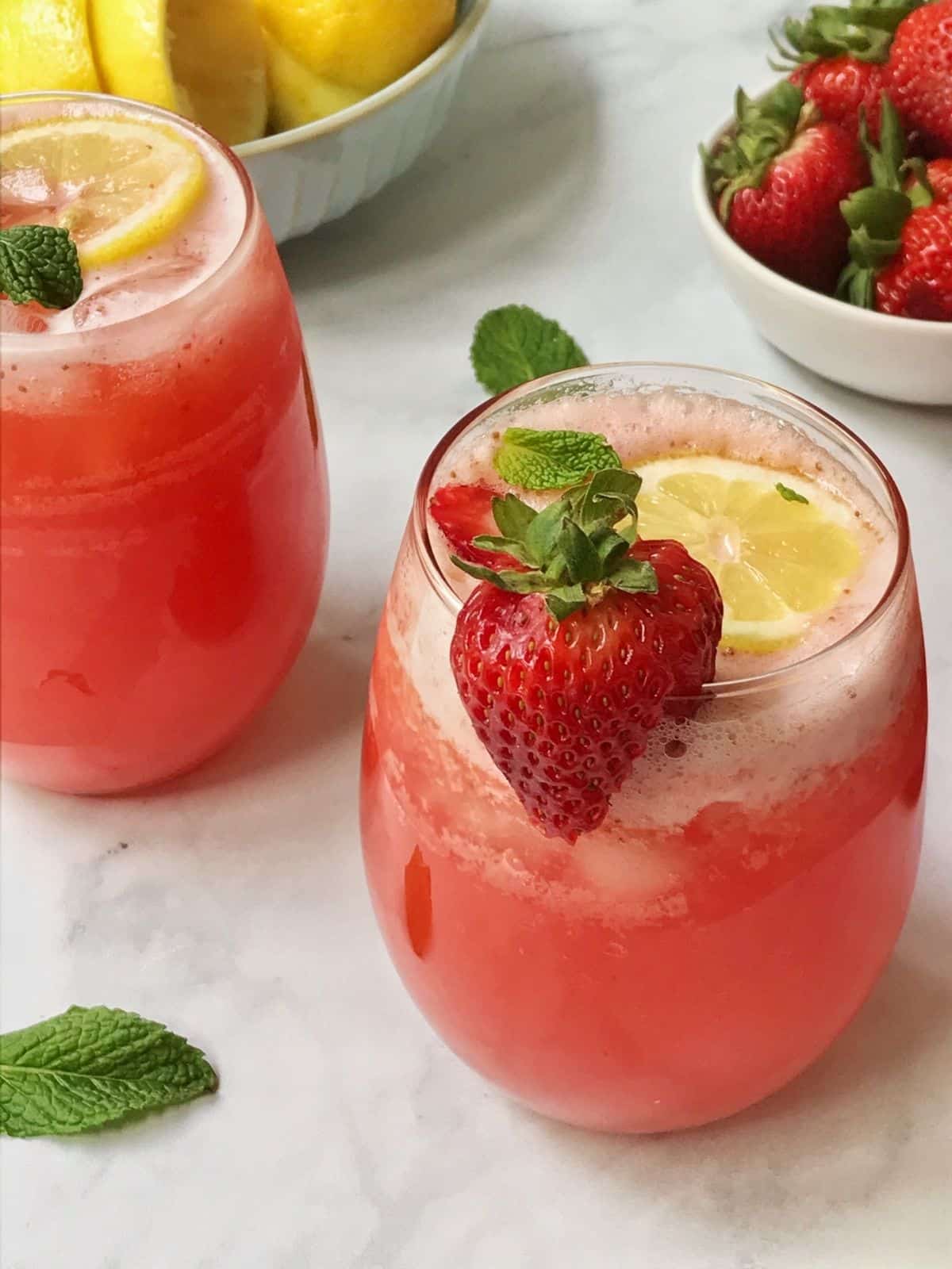 glass of lemonade with bowl of strawberries and lemons in the background