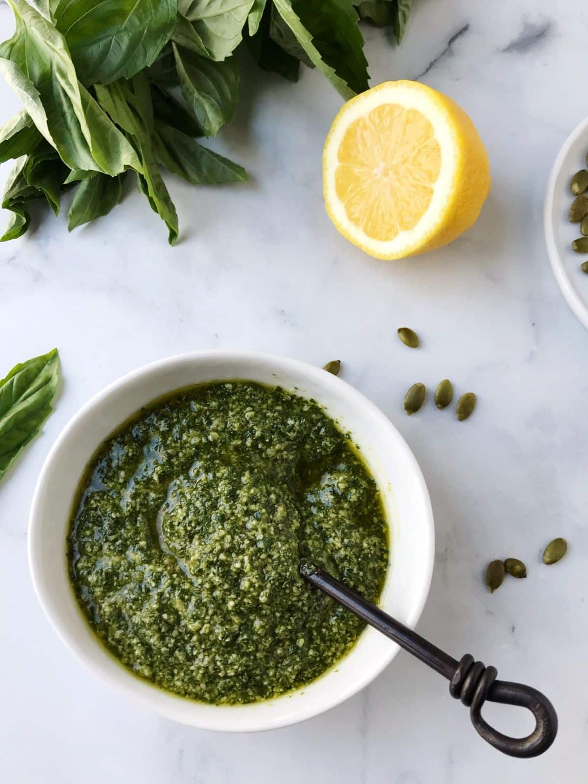 overhead shot of dish of pesto with basil leaves and lemon on the side