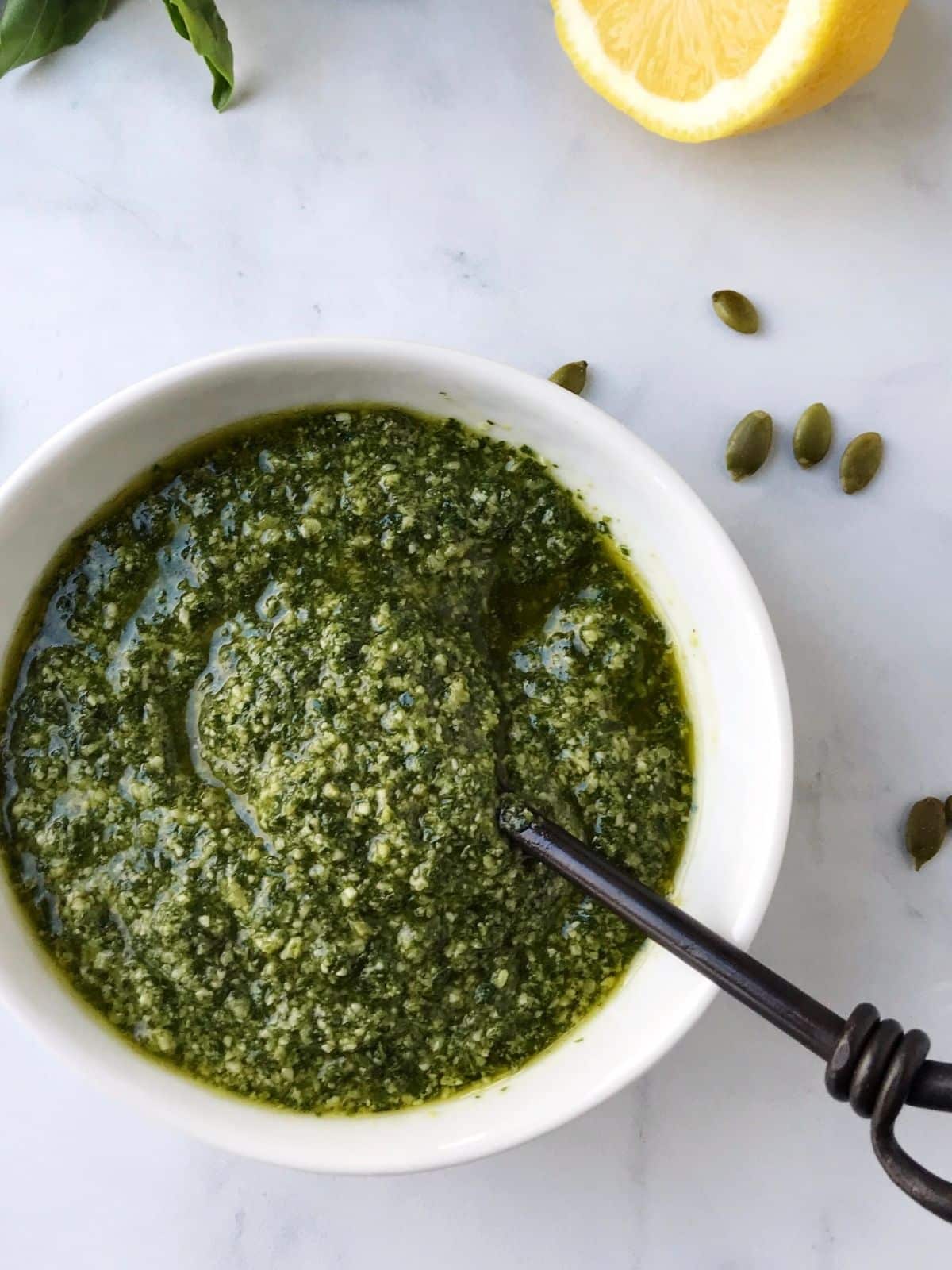 small spoon in dish of pesto with a few pepitas scattered on the side