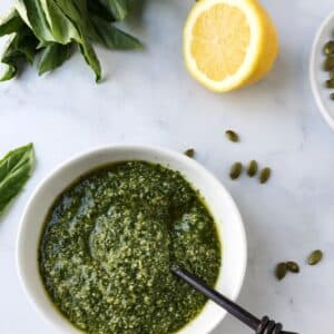 spoon in a bowl of pesto with half of a lemon on the side