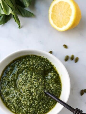 spoon in a bowl of pesto with half of a lemon on the side