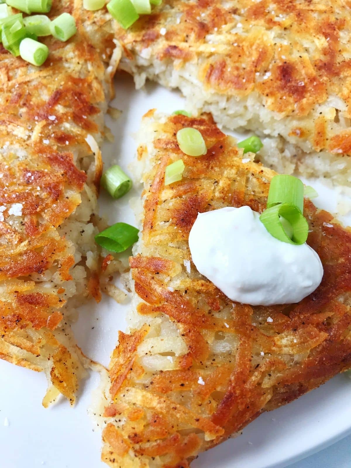 close up of a slice of hash brown topped with sour cream and scallions