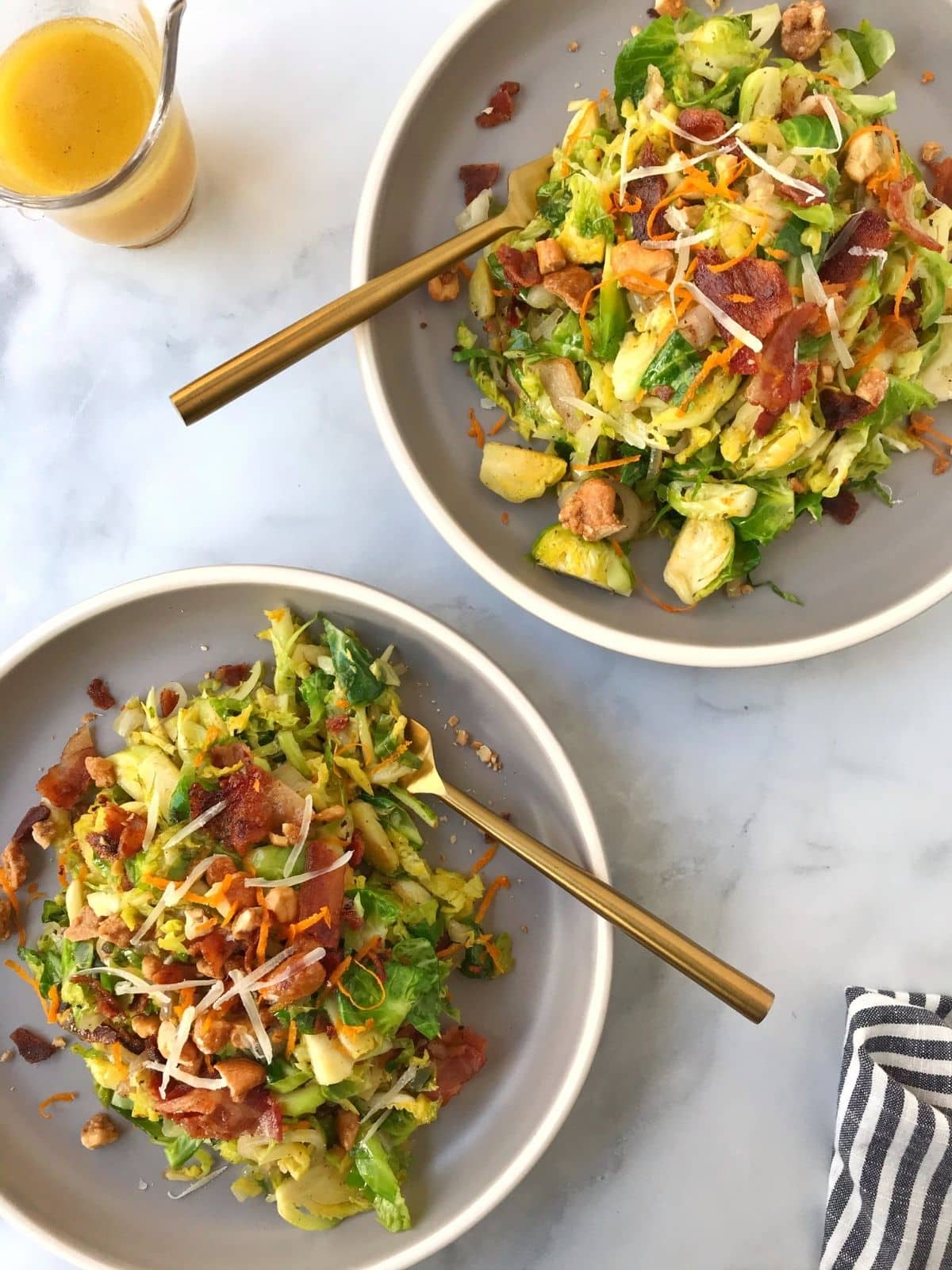 two plates of salad with forks and extra dressing on the side