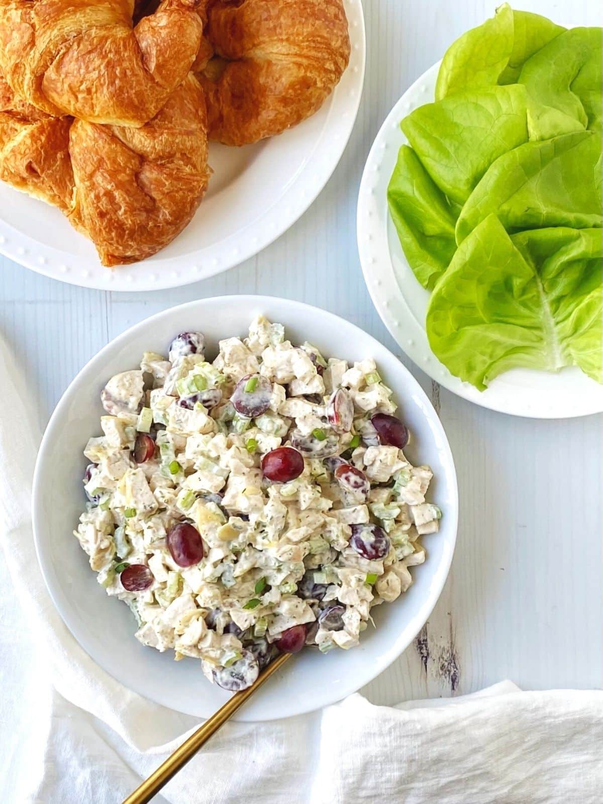 bowl of chicken salad with a plate of croissants and lettuce for building sandwiches