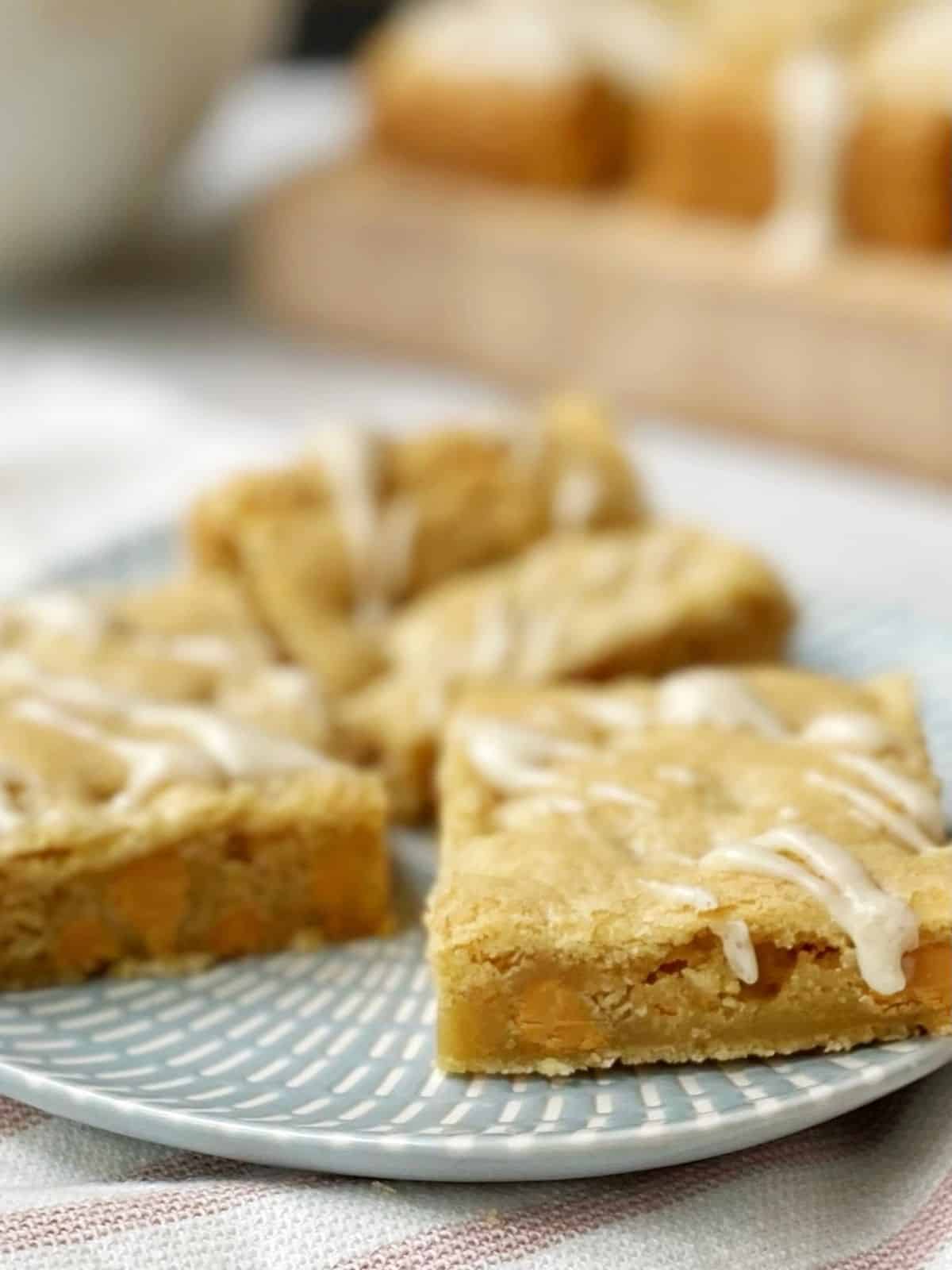 sideview of cookie bars on a plate with more bars on a board in the background