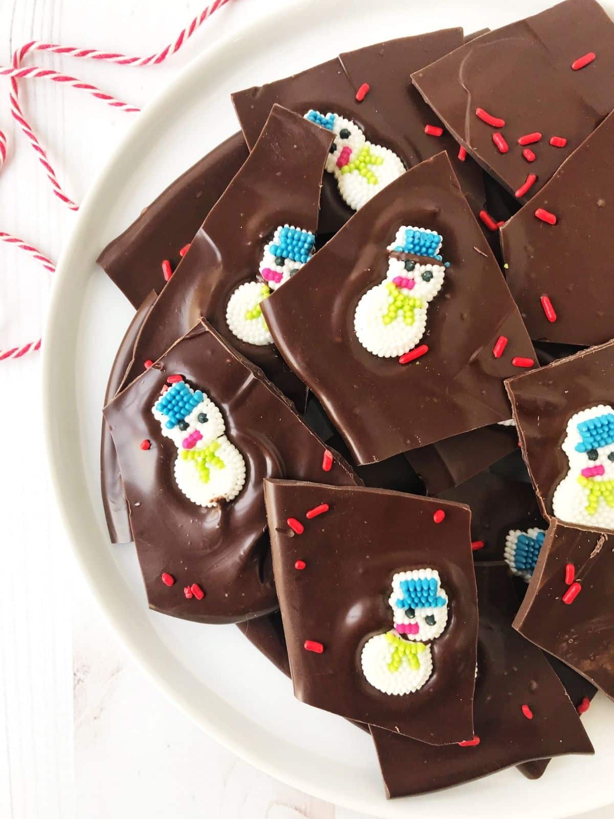 chocolate bark adorned with candy snowmen on a white plate