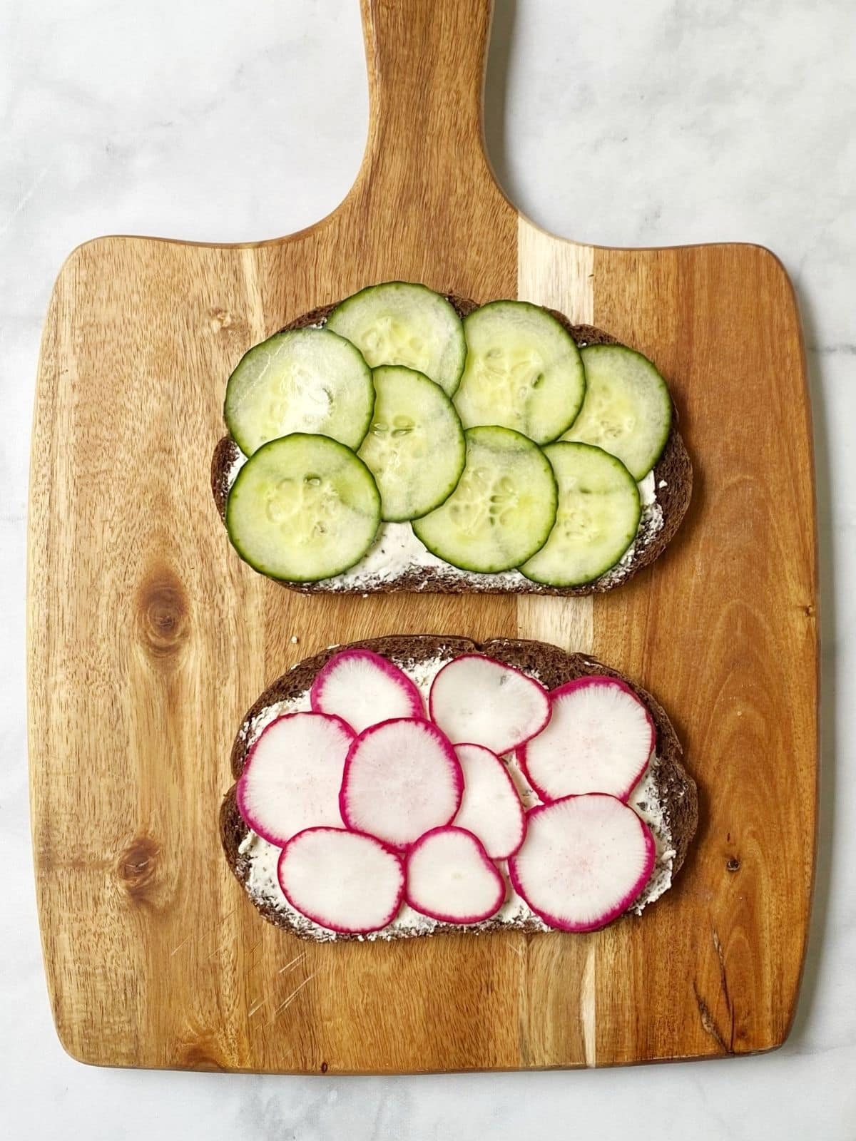 two slices of bread topped with cheese spread; one topped with cucumber and the other with radish