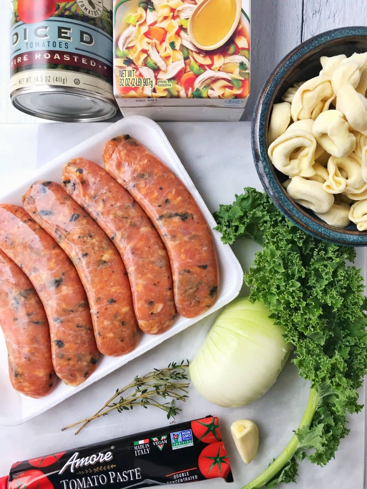 array of ingredients - sausage, kale, pasta, onion, garlic, herbs, tomato paste, stock, tomatoes