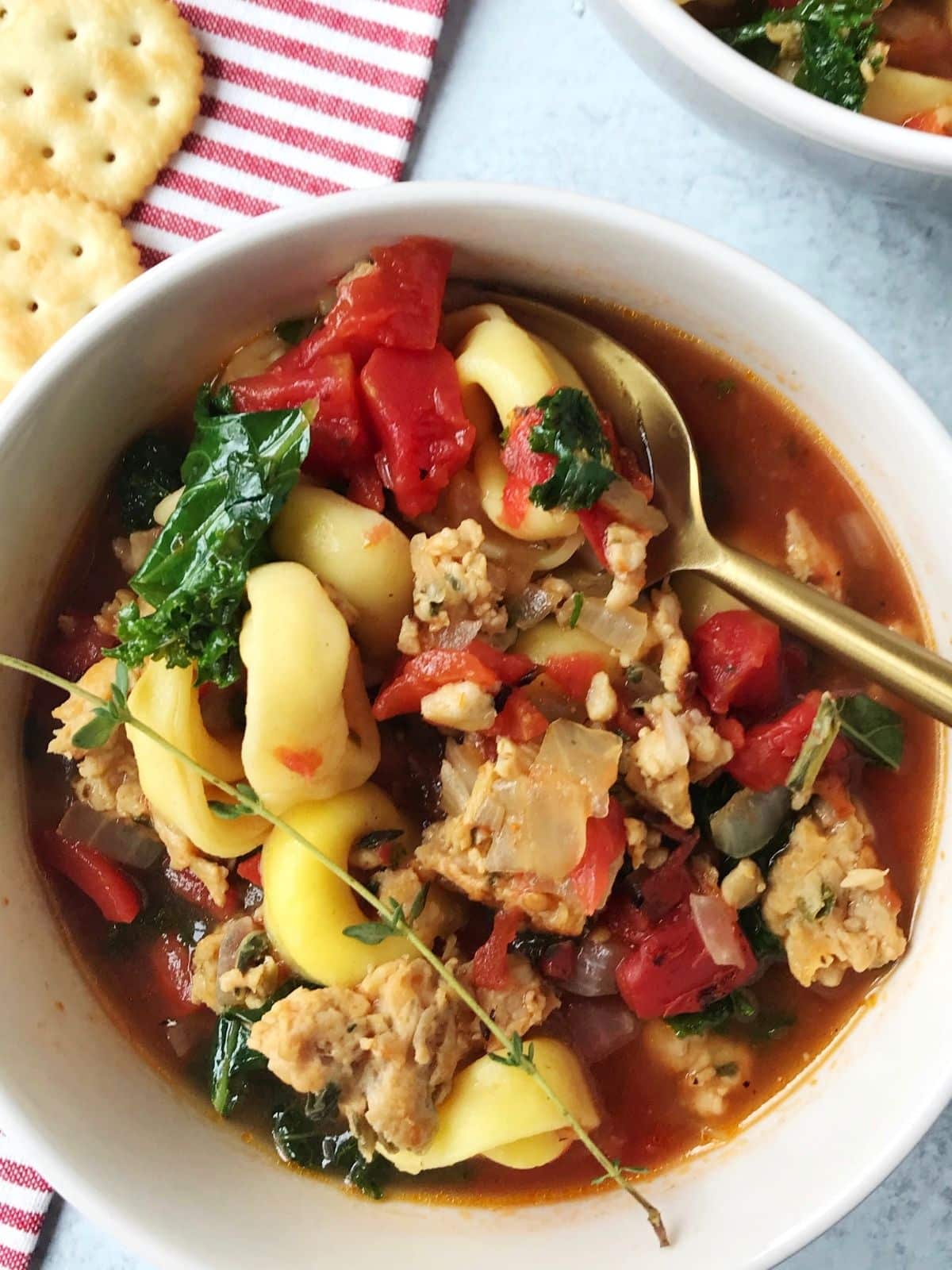 spoon in a bowl of soup with crackers laying next to the bowl