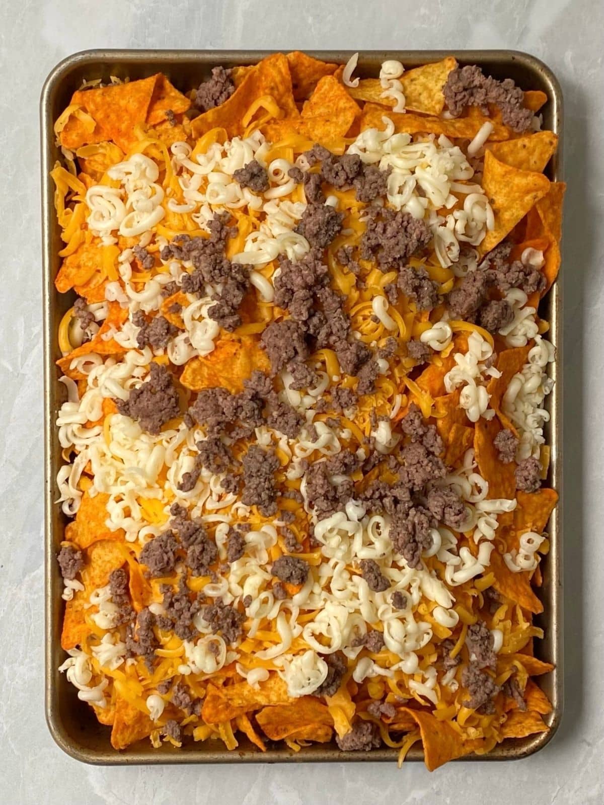 top down shot of Doritos, cheese, and beef layered in sheet pan.