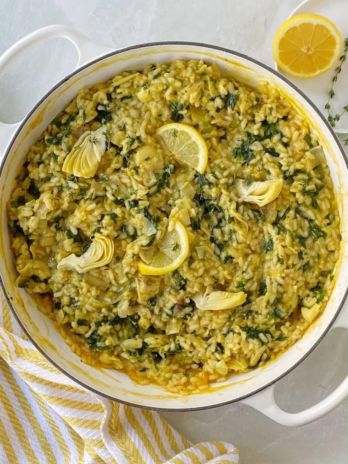 skillet of spinach artichoke risotto garnished with lemon.