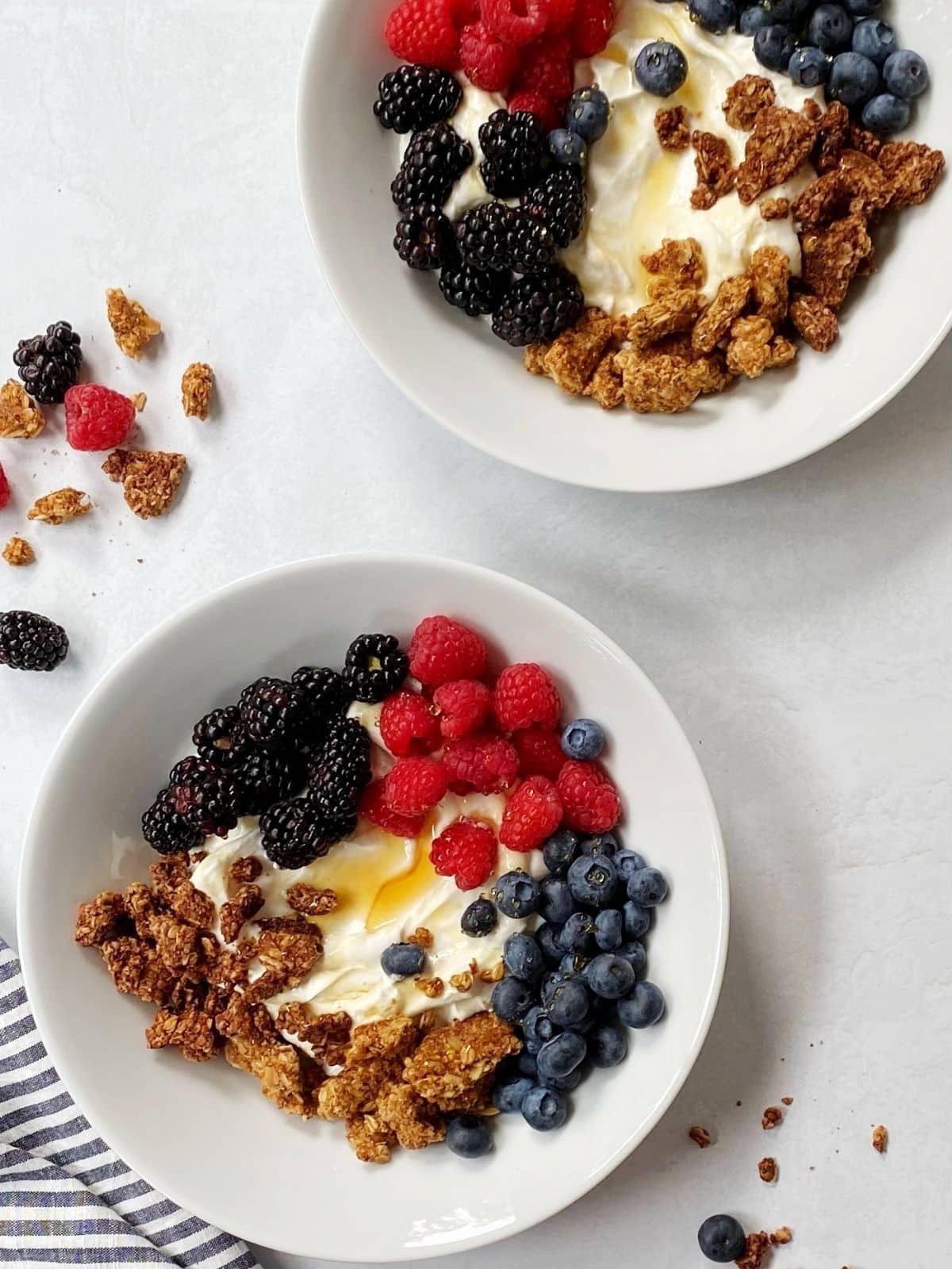 two bowls of greek yogurt with berries and granola.