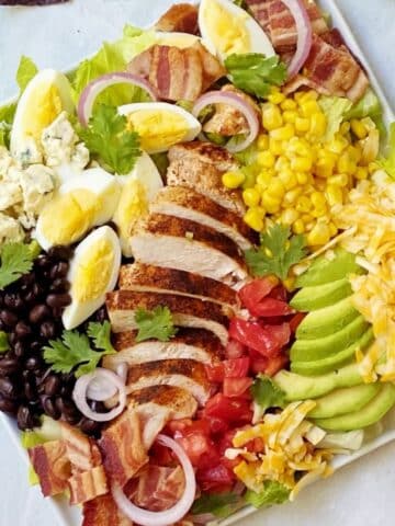 cobb salad on a square white plate with dressing on side.