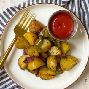 fork on a plate of roasted potatoes with ketchup.