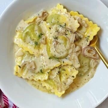 white bowl of ravioli tossed in sauce.