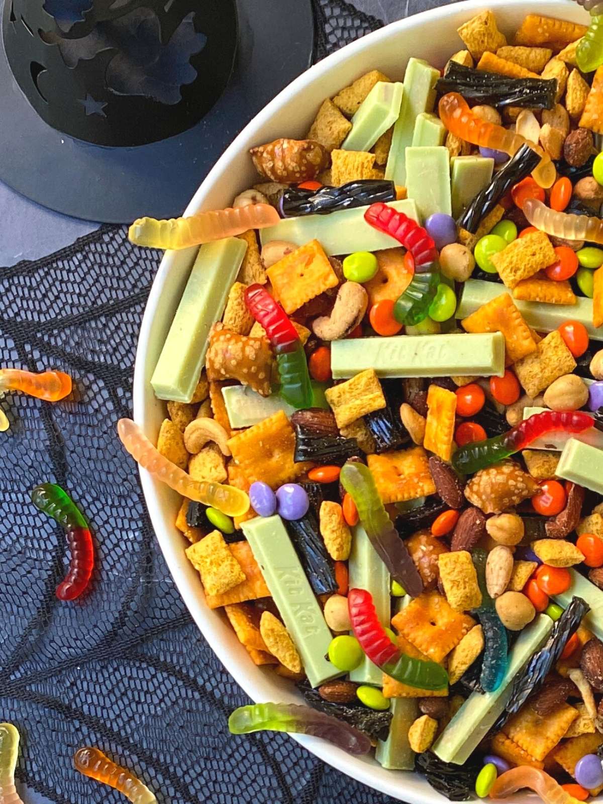 bowl of snack mix offset next to gummy worms and witch hat.