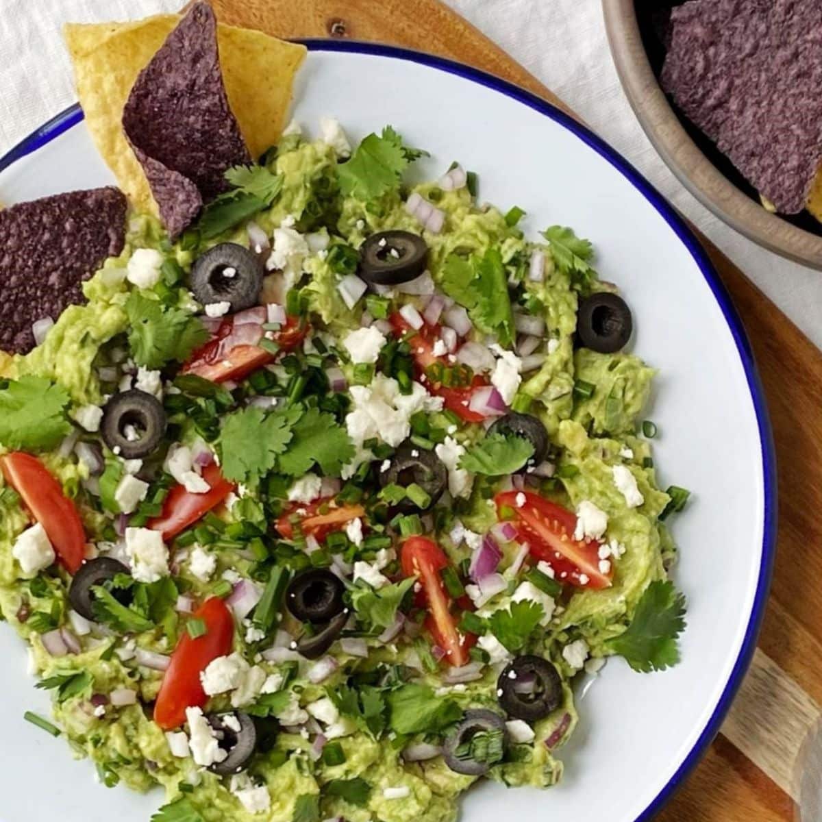 top down shot of plate of loaded guacamole next to bowl of chips.