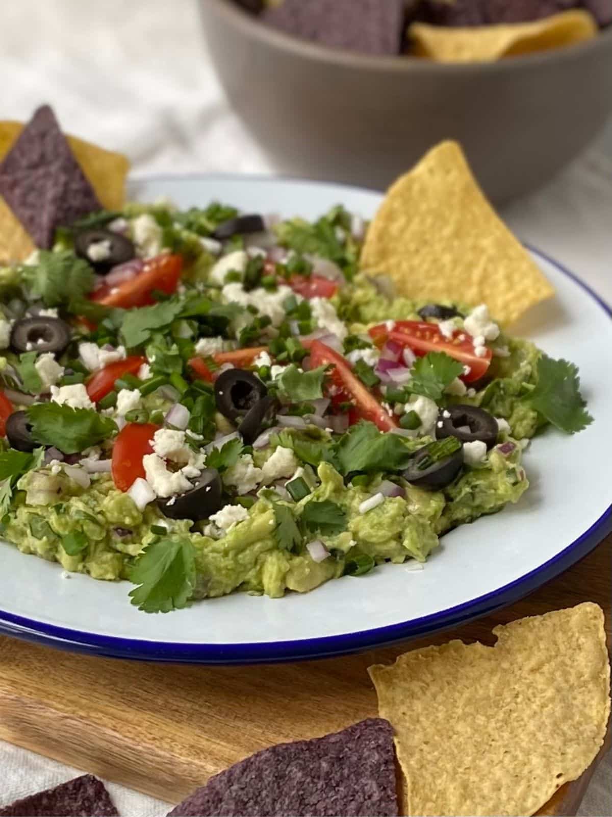 side view of plate of loaded guacamole with chips in background.