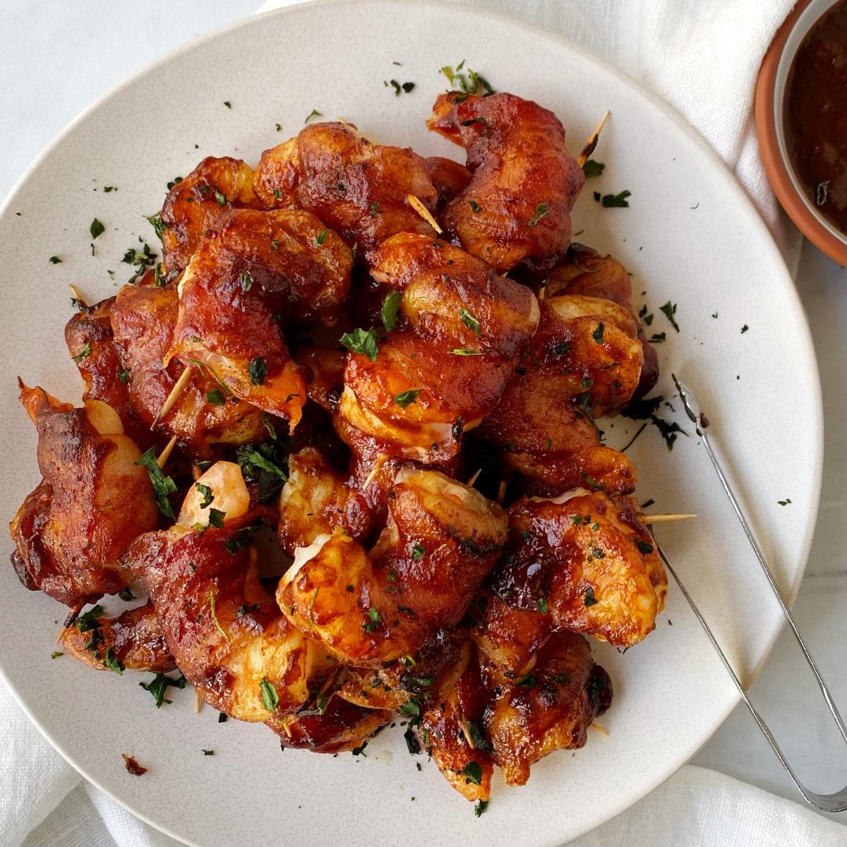 BBQ shrimp on a plate next to a bowl of extra sauce.