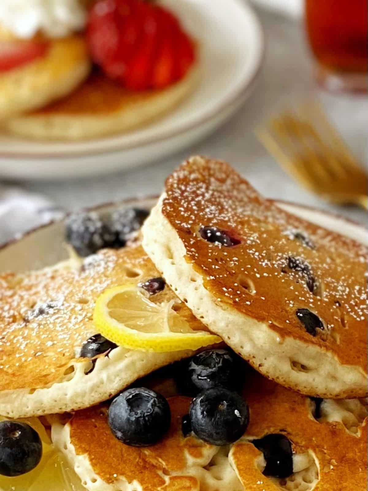 close up of lemon blueberry pancakes with strawberry pancakes in the background.
