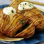 close up side view of hasselback potatoes topped wth sour cream.