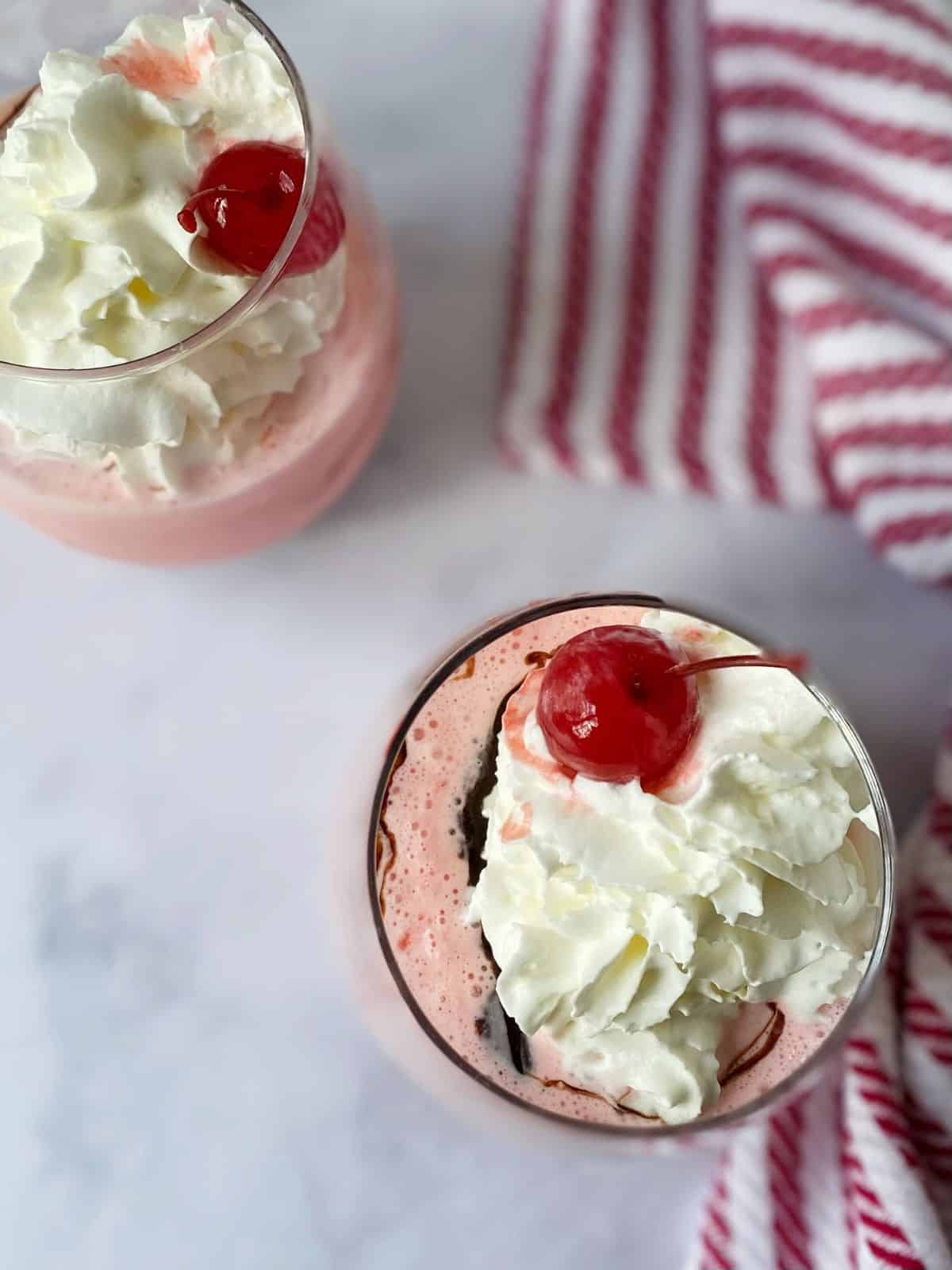 milkshake in glasses topped with whipped cream and cherries.