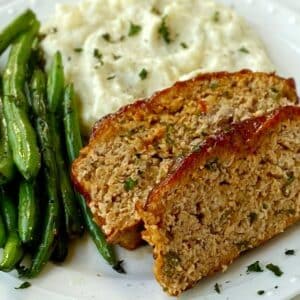 white plate with meatloaf, mashed potatoes, and green beans.