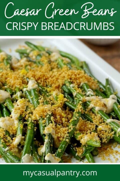 close up of green beans on a white platter topped with dressing and breadcrumbs.