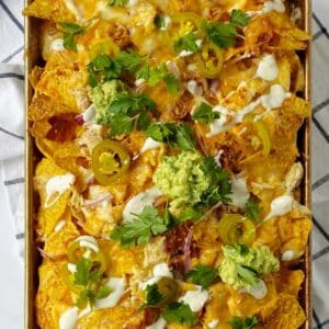 sheet pan of chicken nachos garnished with cilantro and guacamole.
