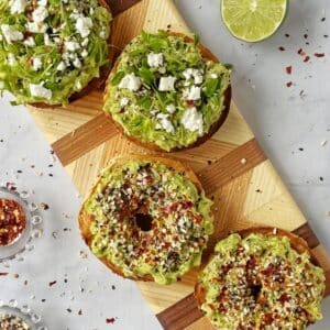 bagels with avocado and toppings on a cutting board.
