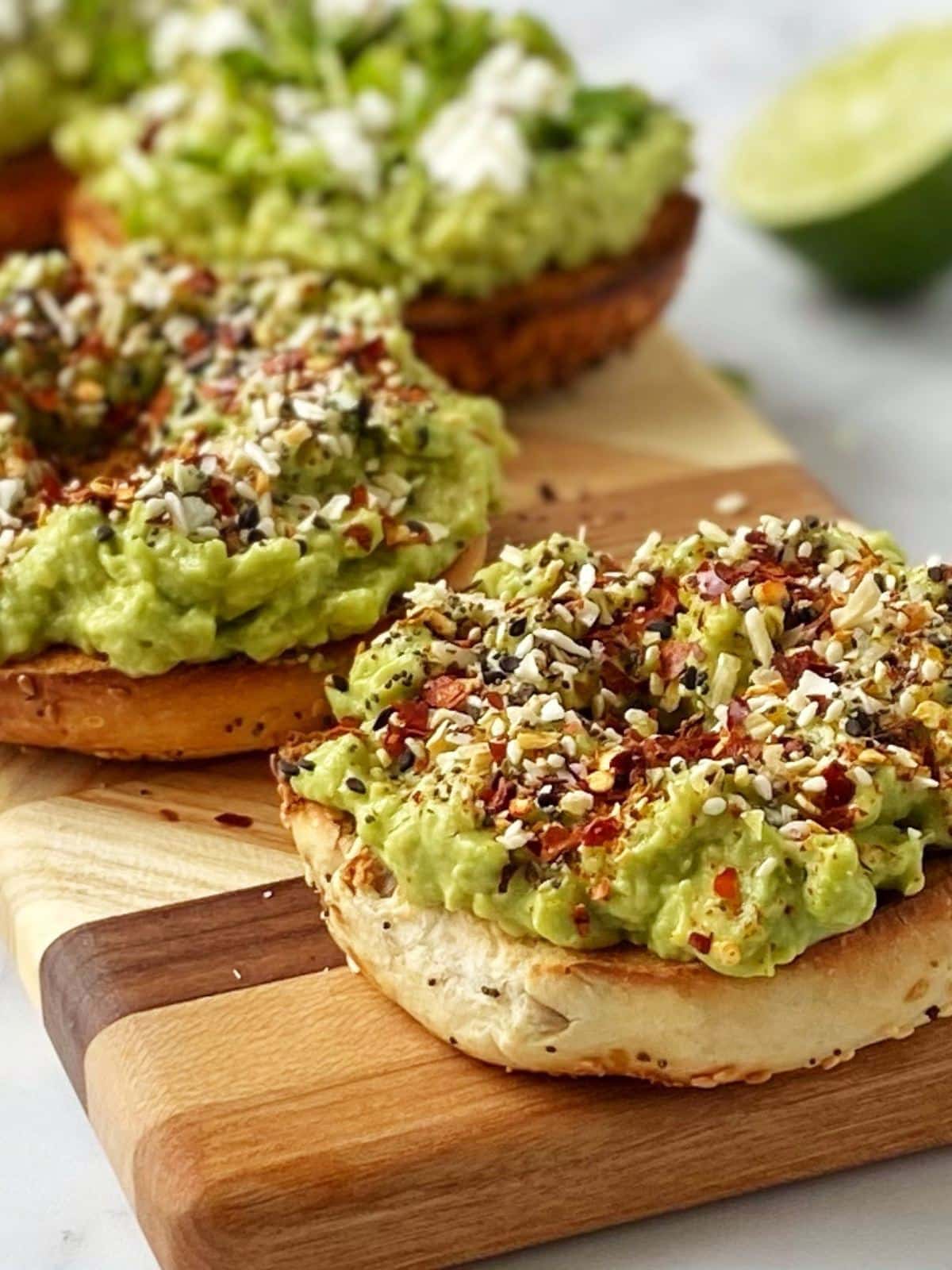 side view of avocado-topped bagels on a cutting board.