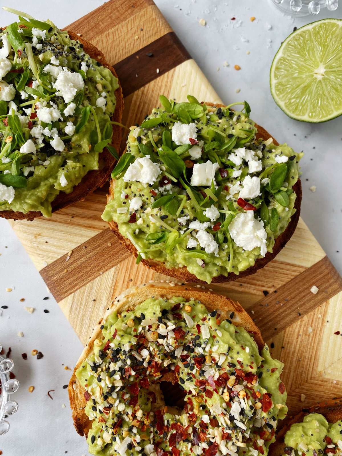 avocado bagel with pea shoots and crumbled feta on a wooden board.