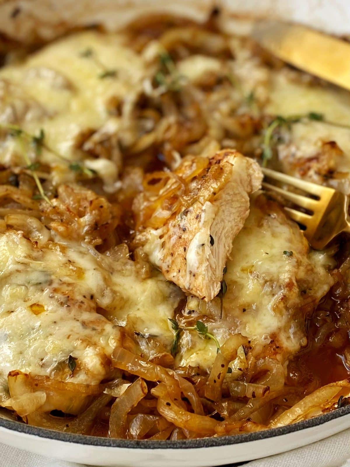 close up of sliced chicken in skillet with onions and melted cheese.
