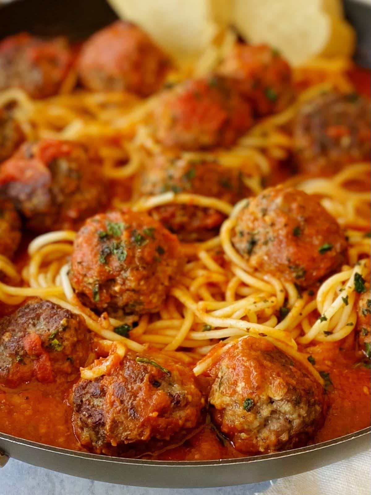 close up side view of meatballs in pasta in skillet.