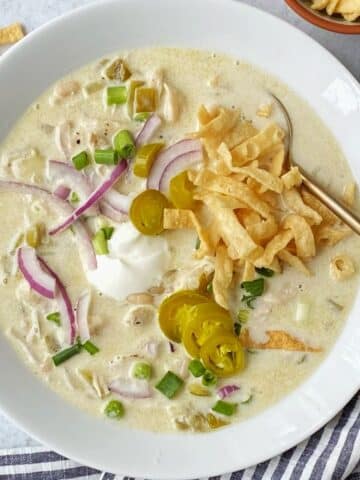 bowl of white chicken chili garnished with red onions, scallions, sour cream, jalapenos, and tortilla strips.