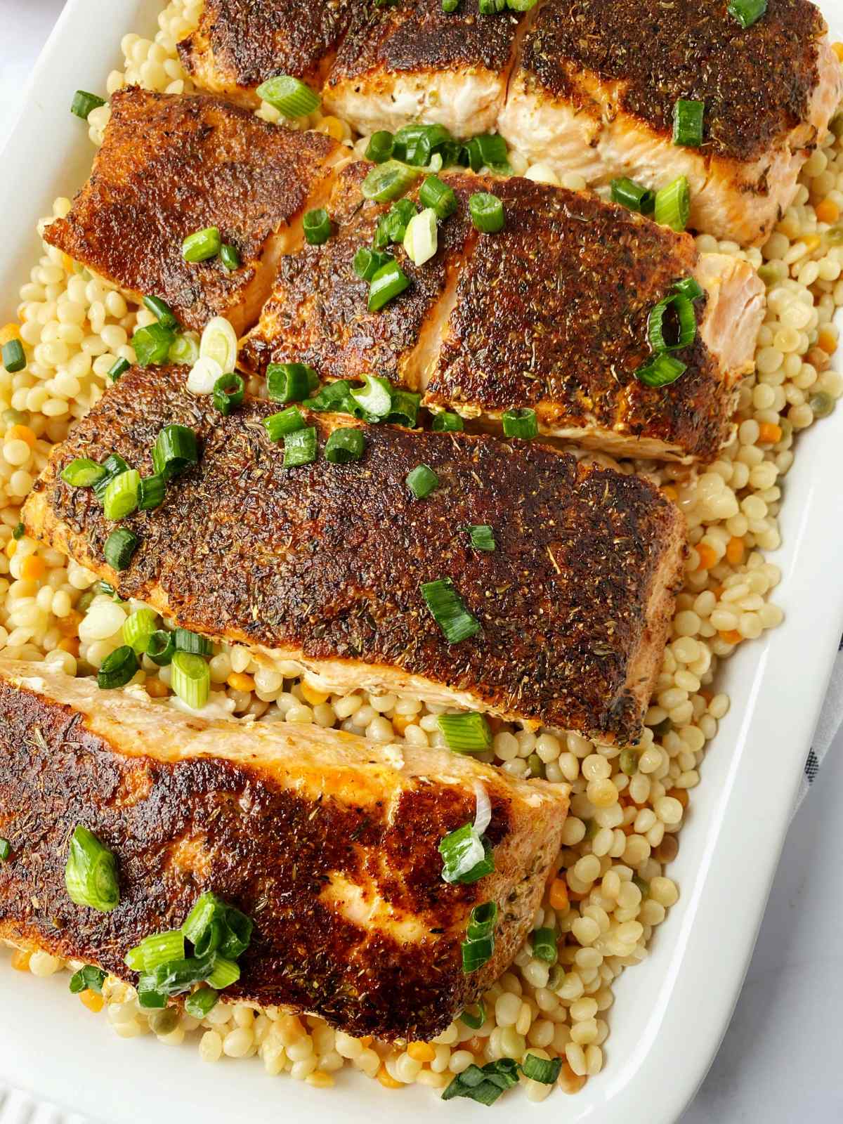 blackened salmon on a bed of couscous on a white platter.