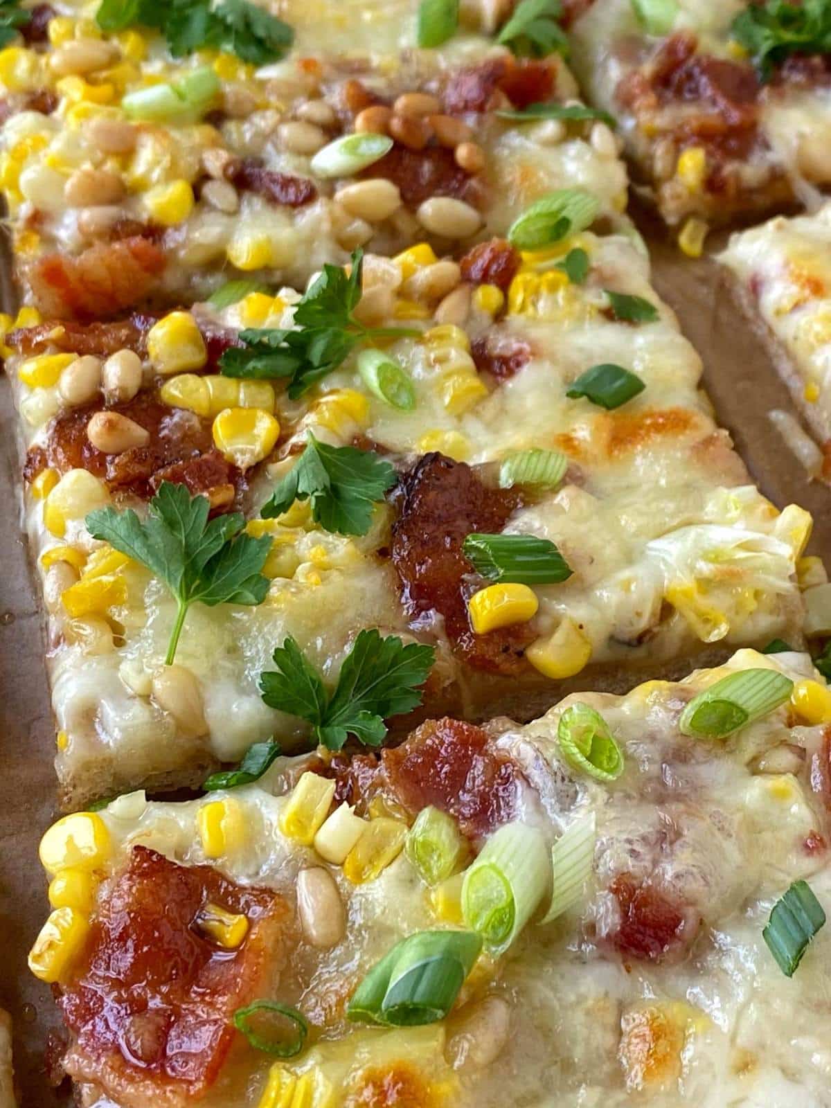 side angle view of sliced corn bacon and pine nut pizza.