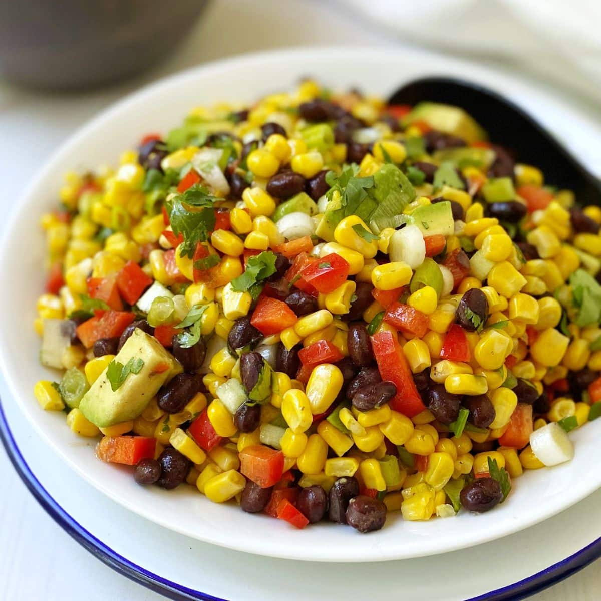 white serving bowl of corn black bean and avocado salad.