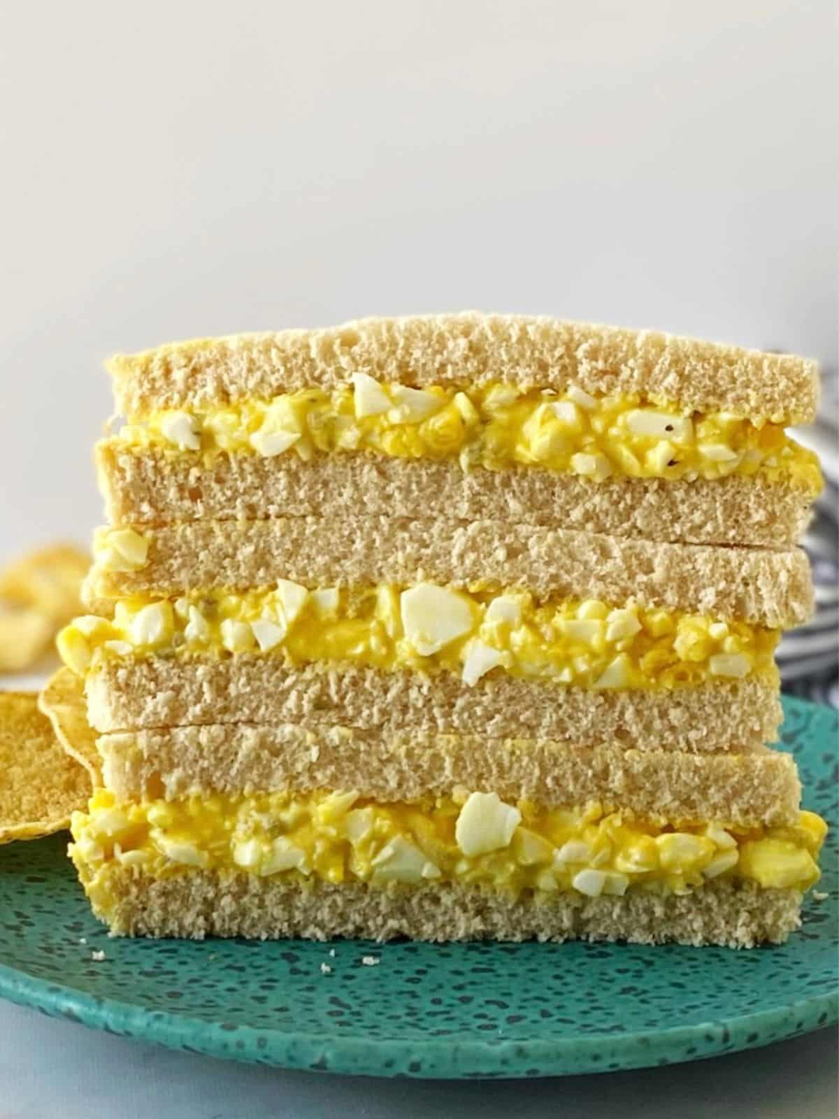 egg salad sandwiches cut in half and stacked on a green plate.