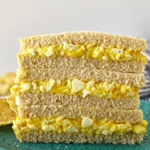 egg salad sandwiches cut in half and stacked together on a plate.